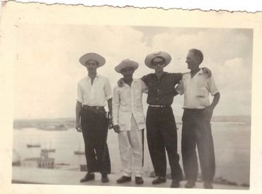 Four men posing together outdoors with hats, vintage style.