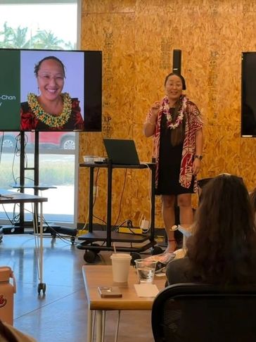 Woman giving a presentation with lei and traditional attire.