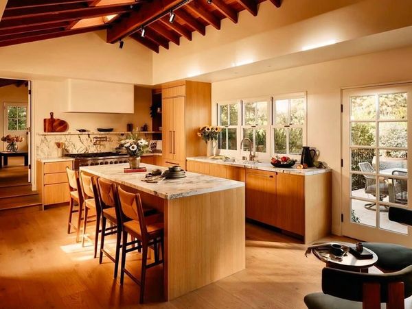 Warm, modern kitchen with wooden cabinetry and marble countertops under a wooden beam ceiling.