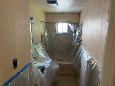 A small room prepared for painting with plastic coverings and taped edges.
