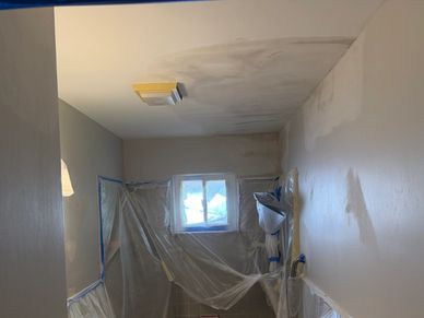 Room being prepped for painting with plastic coverings and taped edges.
