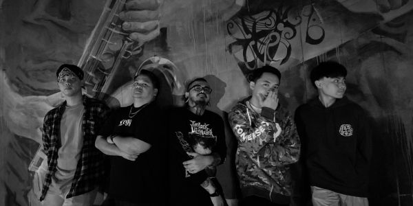 Five young men posing against a graffiti wall in black and white.