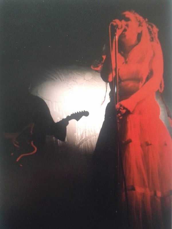 Silhouetted guitarist and red-lit singer performing on stage.