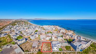 Aerial view of a coastal residential area with a vacant lot outlined in red.