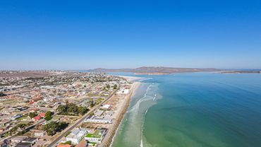 Coastal town with houses lining a sandy beach under a clear blue sky.