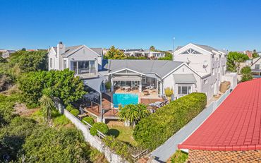 Large modern house with a pool and lush greenery under a clear blue sky.