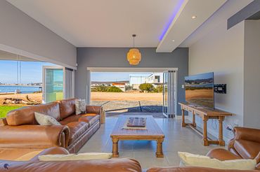 Modern living room with leather sofas and large open windows overlooking a scenic outdoor area.