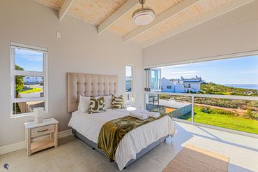 Bright bedroom with large windows overlooking greenery and distant buildings.