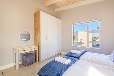 Bright bedroom with twin beds, blue throws, and a wooden wardrobe.
