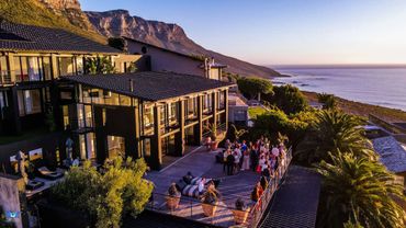 A coastal villa with a crowd enjoying sunset on a spacious deck overlooking the ocean.