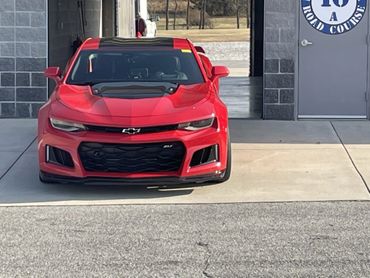 Front view of a red Chevrolet Camaro ZL1 parked outside a garage.
HPDE