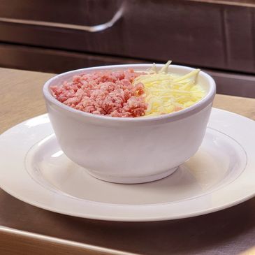 Bowl with finely minced meat and shredded cheese on a white plate.