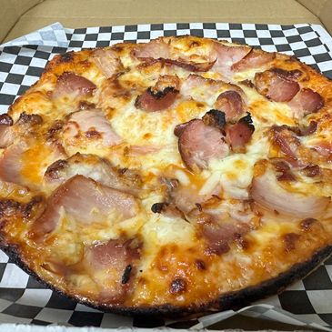 Close-up of a cheesy ham pizza with a crispy crust on checkered paper.