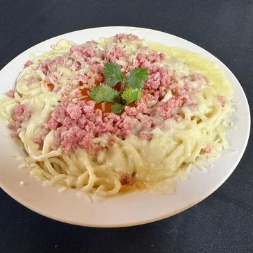 Plate of spaghetti with melted cheese, ground meat, and a garnish of herbs.