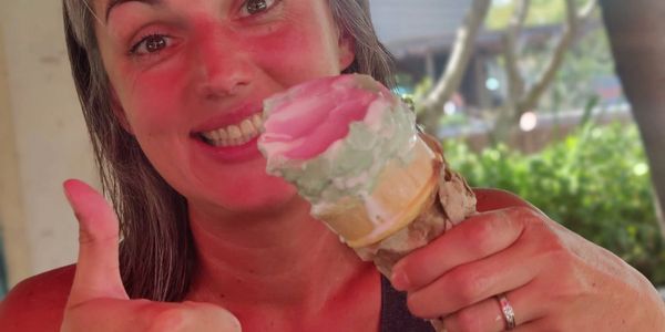 Happy woman holding a colorful ice cream cone and giving a thumbs up.