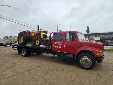 Red tow truck carrying a vintage yellow Minneapolis-Moline tractor.