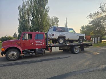 Red tow truck carrying a white vintage SUV on a sunny day.