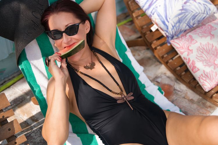 Woman lounging in black swimsuit eating watermelon black sunglasses butterfly dragonfly necklaces