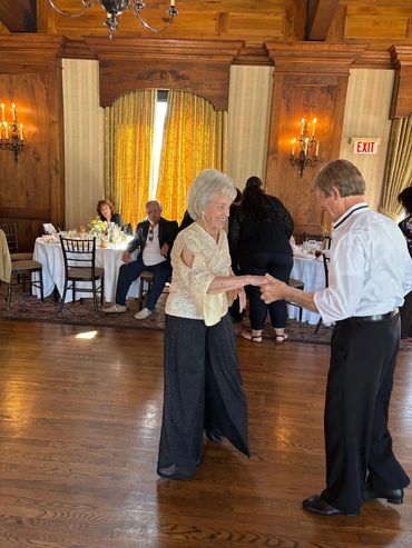Elderly couple dancing joyfully in an elegant room with wooden decor.