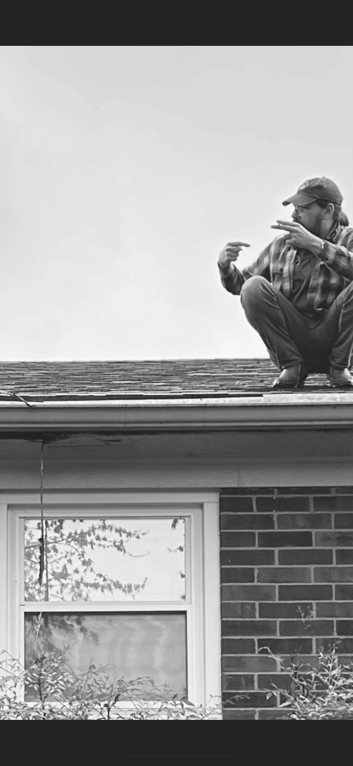 Man squatting on a rooftop, pointing at something off-frame.