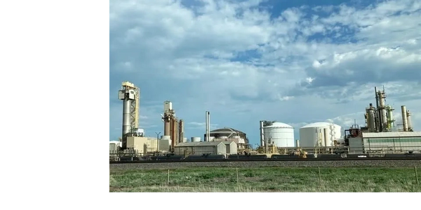 Industrial refinery complex with large storage tanks under a partly cloudy sky.