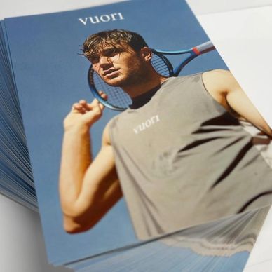 Stack of glossy promotional postcards featuring a fashion model holding a tennis racket printed in v