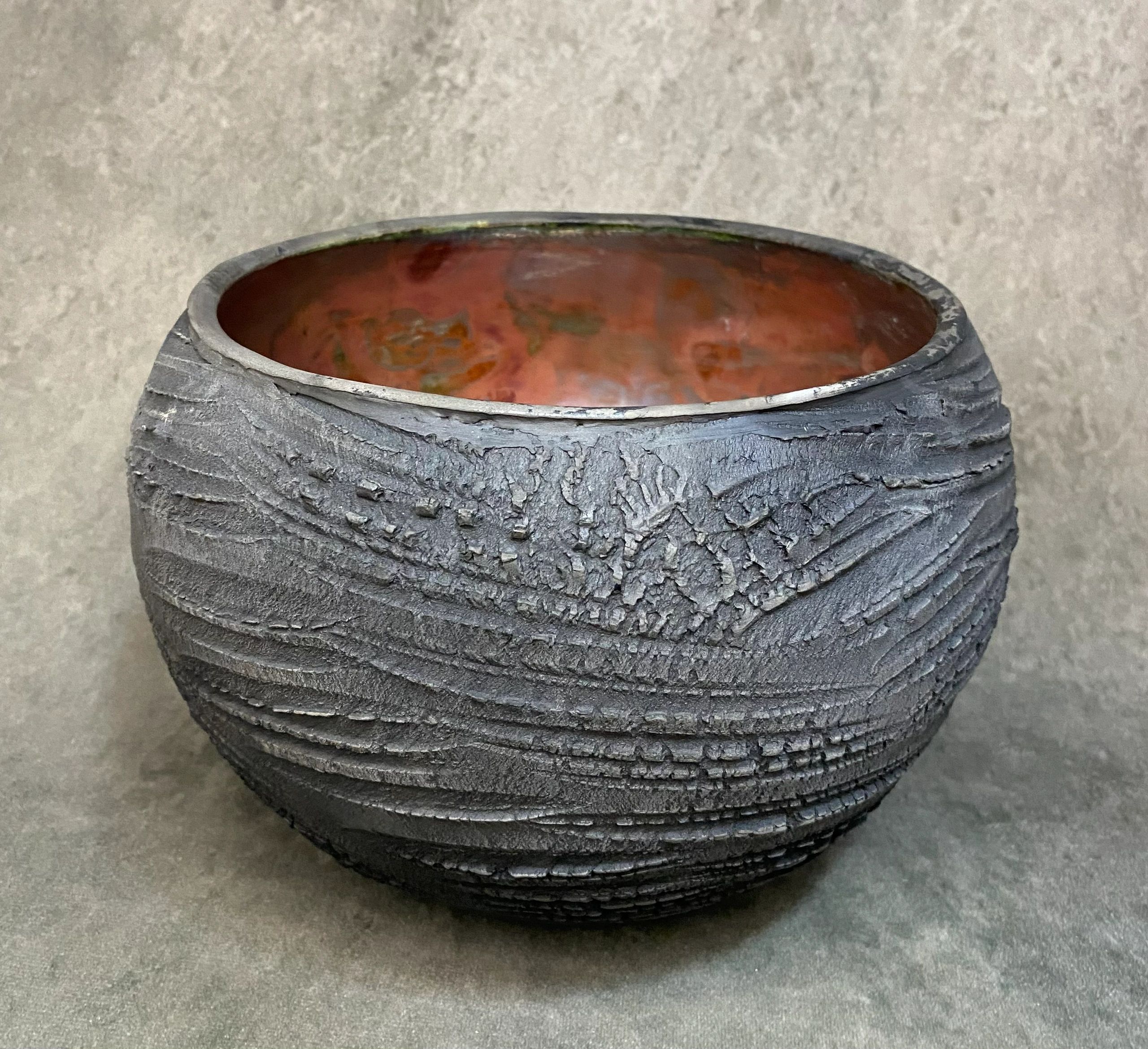 Round textured ceramic bowl with a dark exterior and reddish interior.