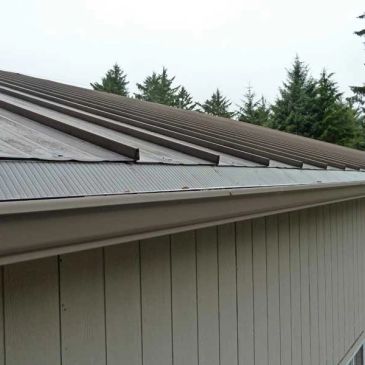 Metal roof with snow guards on a building under cloudy sky.