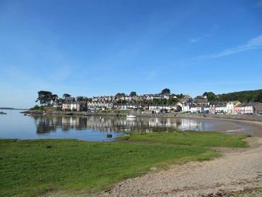 Coastal village with houses reflected in calm water under a clear blue sky.