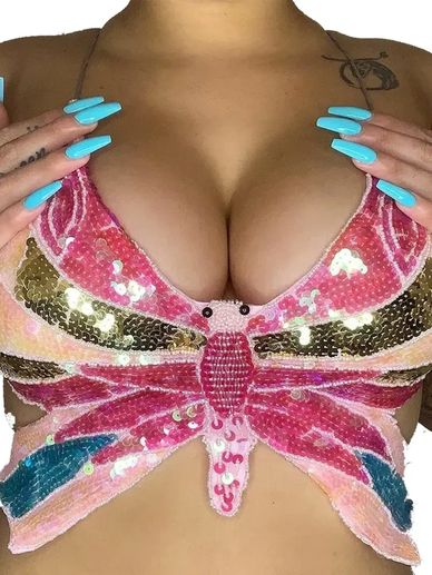 Woman wearing a colorful sequin butterfly top with long blue nails.