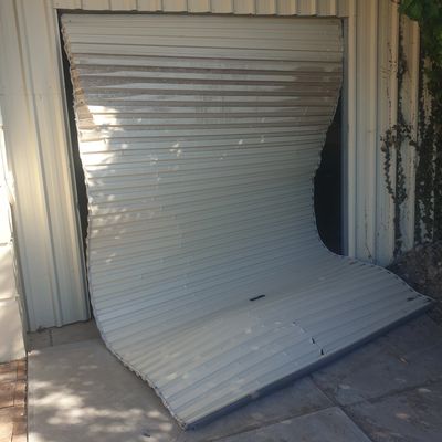 A severely bent metal roll-up door detached from its frame.