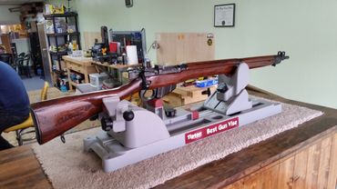 A wooden rifle secured in a Tipton gun vise inside a workshop.