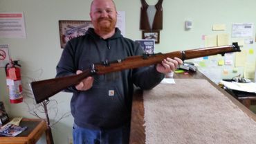Man holding a vintage wooden rifle indoors at a counter.