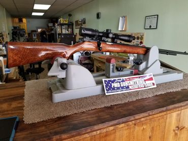 A hunting rifle with a scope on a gun rest in a gunsmith shop.