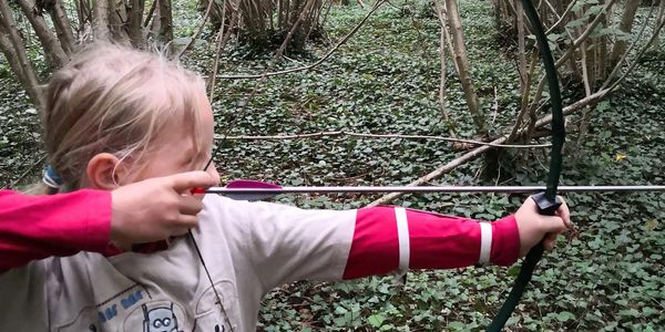 Child in forest with bow and arrow aimed.
