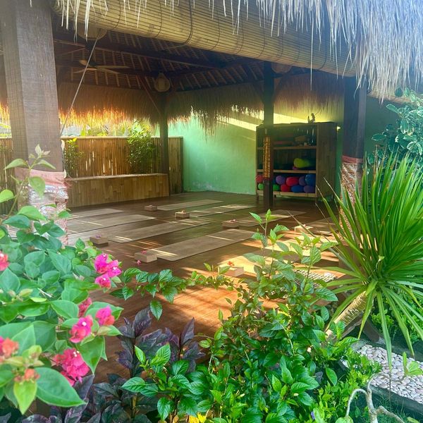 Outdoor traditional yoga shala with mats and blocks under an alang alang roof surrounded by lush, tropical garden.
