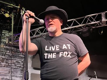 Mel Stahler, lead vocals in Lynyrd Skynyrd tribute band Freebyrd holding mic stand on stage