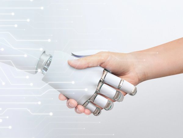 A human hand shaking hands with a robot hand, with digital lines in the background.