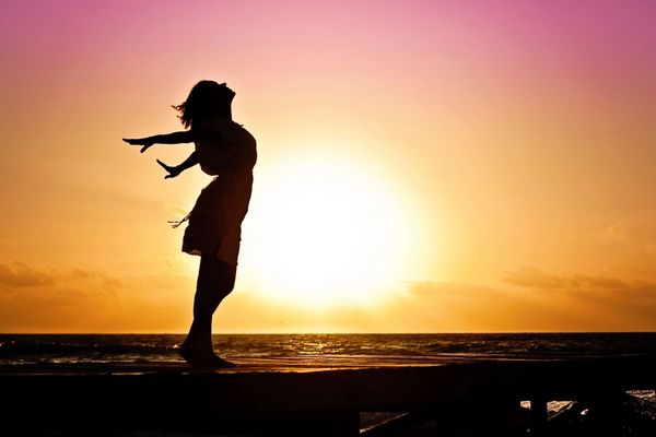 Woman embracing sunset by ocean.