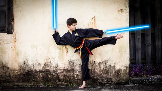 Boy in martial arts pose holding lightsabers.