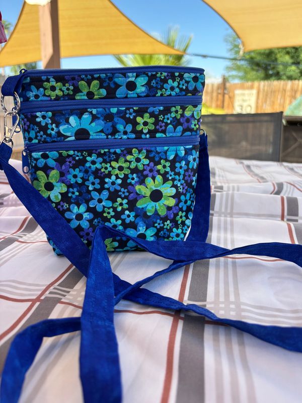 Blue floral patterned bag with a strap on a bed.