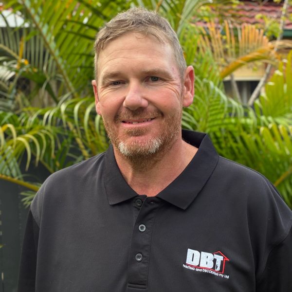 Man in black DBT shirt smiling outdoors.