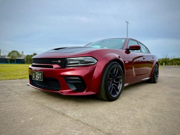 A red Dodge Charger SRT with black hood and custom license plate parked outdoors.
