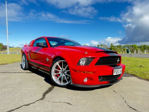 Red Ford Mustang Shelby GT500 parked on a sunny day with blue skies.