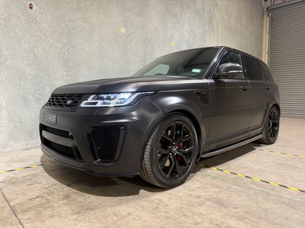 Matte black luxury SUV parked indoors with sleek design and glowing headlights.