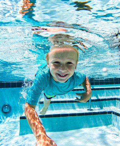 Smiling boy swimming underwater in a pool, wearing a blue shirt.