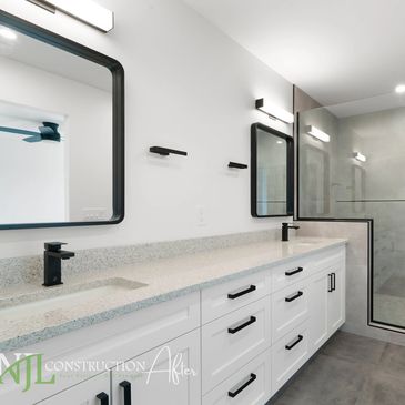 Bathroom with doubles sinks, white cabinetry, large grey tiles and walk in shower