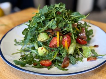 Fresh arugula salad with avocado, cherry tomatoes, and bacon bits.