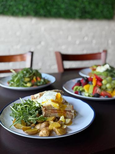 A breakfast plate with sandwich, fried potatoes, and arugula greens.