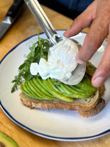 Adding a poached egg on avocado toast with arugula on a plate.